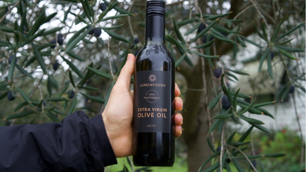 Person holding a bottle of olive oil in front of an olive tree