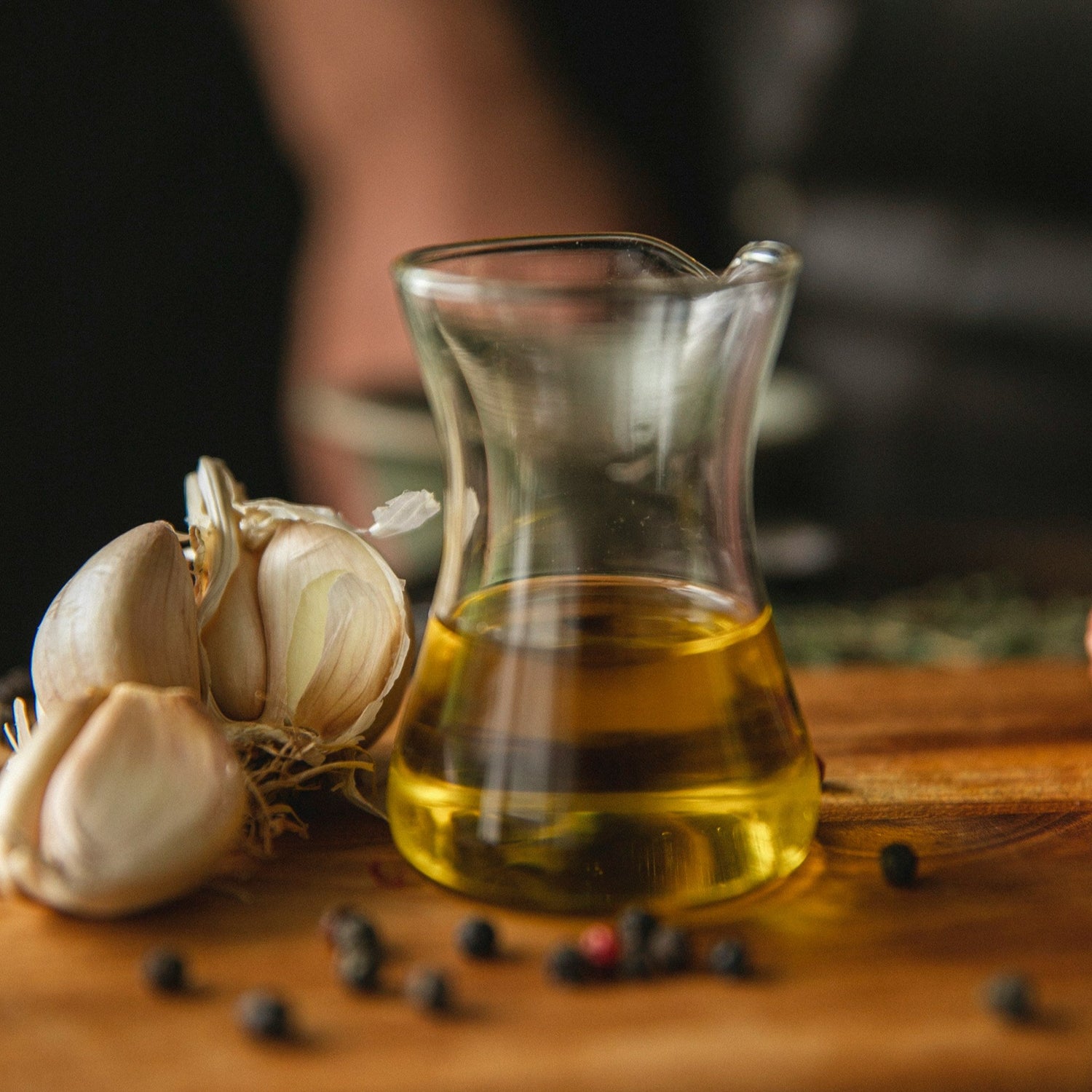 Glass container of oil with garlic and peppercorns on a wooden surface