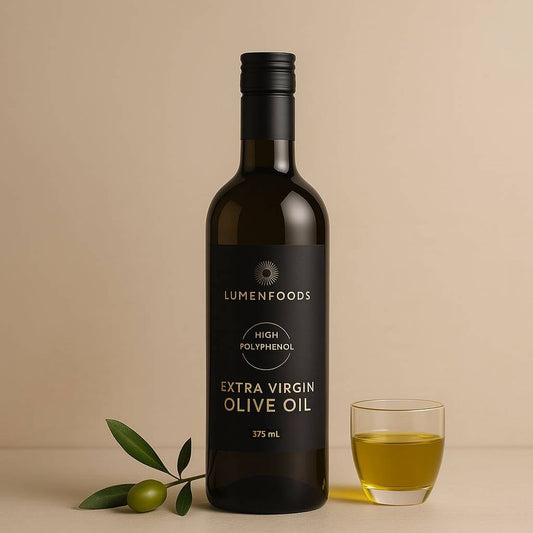 Bottle of Lumenfoods Extra Virgin Olive Oil with a glass and olives on a beige background