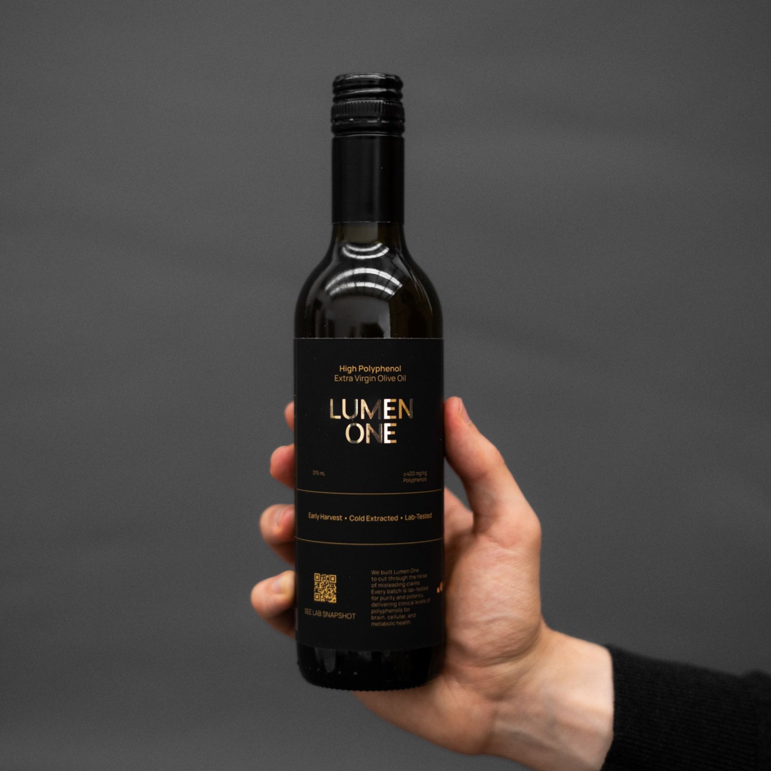 Hand holding a bottle of Lumen One olive oil against a dark background