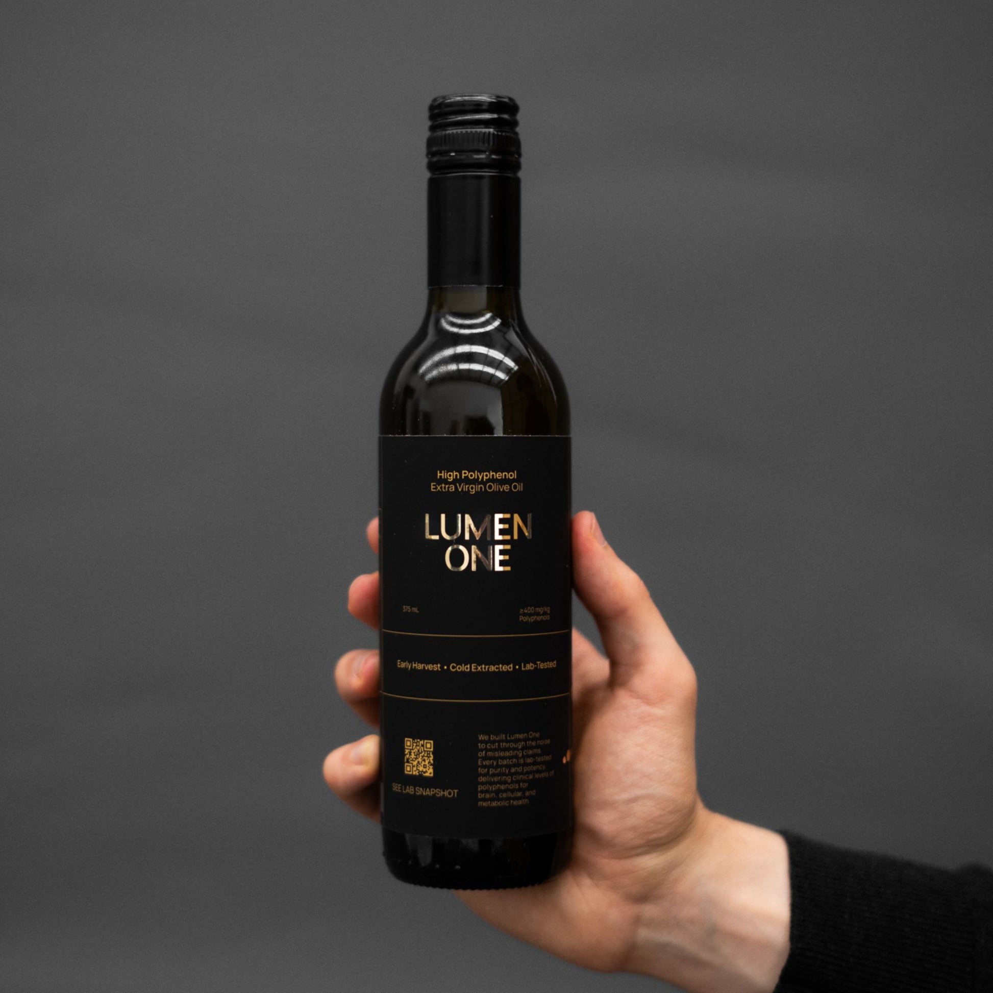 Hand holding a bottle of Lumen One olive oil against a dark background