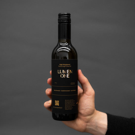 Hand holding a bottle of Lumen One olive oil against a dark background