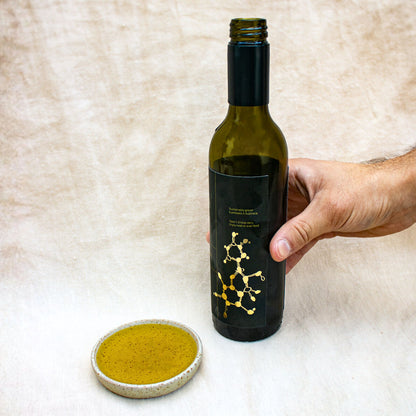 Bottle of Lumen One high polyphenol olive oil with a hand holding it, next to a small dish of olive oil on a textured beige background.